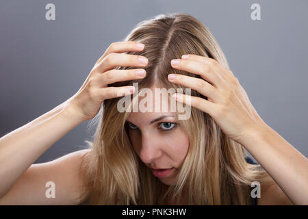 Jeune femme blonde l'examen de ses cheveux sur fond gris Banque D'Images