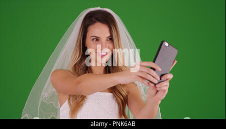 Mariée en robe de mariée et voile en tenant un téléphone cellulaire avec selfies sur écran vert Banque D'Images