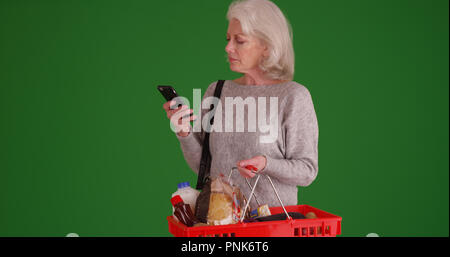 Vieille femme blanche à l'épicerie à l'aide de téléphone sur un écran vert Banque D'Images