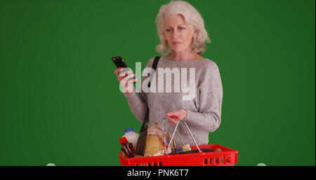 Vieille dame à la recherche sur la valeur nutritive téléphone pendant des courses sur écran vert Banque D'Images