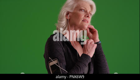 Athletic senior female mettre des écouteurs avant d'aller sur jog sur écran vert Banque D'Images