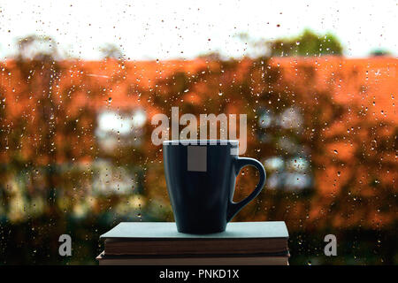 Livres et café sur la fenêtre, la pluie tombe sur le verre en arrière-plan Banque D'Images