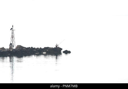 Silhouette de pêcheur avec des cannes à pêche et le phare sur la jetée. Le minimalisme. Banque D'Images
