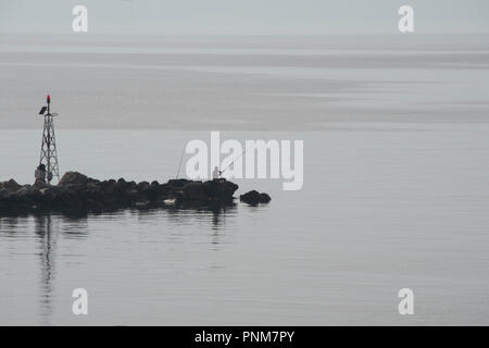 Silhouette de pêcheur avec des cannes à pêche et le phare sur la jetée. Le minimalisme. Banque D'Images