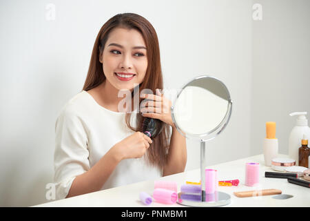 Se débarrasser d'écheveaux. Belle jeune femme regardant son reflet dans mirrorand brosser ses longs cheveux tout en restant assis à la coiffeuse Banque D'Images