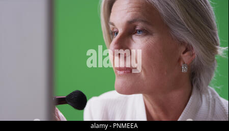 Belle mature woman applying makeup sur greenscreen Banque D'Images