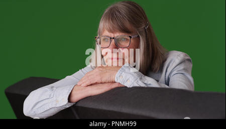 Sad senior femme blanc tête de repos assis sur la table sur un écran vert Banque D'Images