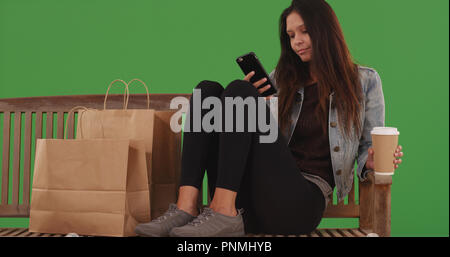 Femme assise sur un banc de travail avec shopping sur écran vert Banque D'Images