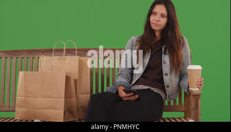 Portrait of Girl sitting on bench with shopping bags et téléphone sur un écran vert Banque D'Images