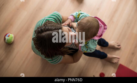 Vue de dessus de jeune mère embrassant amoureusement sa petite fille comme elle s'assoit sur ses genoux. Banque D'Images