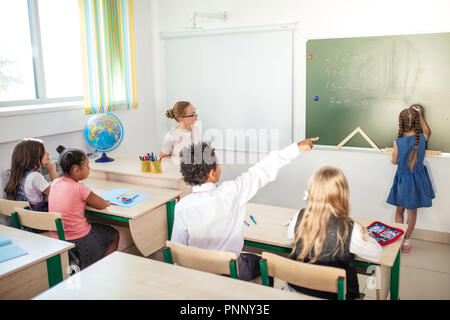 Avec l'enseignant en classe écolier. Tableau fille près de montrer ses devoirs Banque D'Images