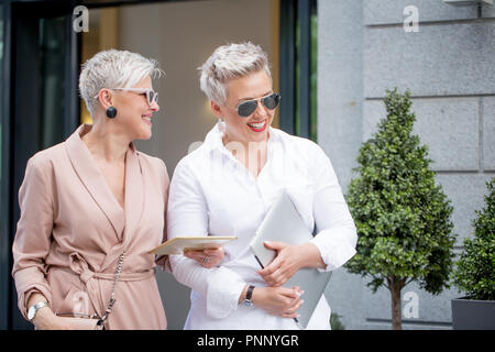 Deux businesswoman walking on street près du bâtiment. Femme d'affaires allant de pair avec l'ordinateur tablette Banque D'Images