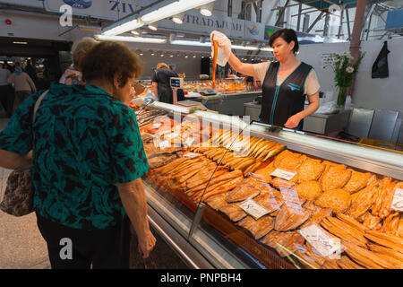 Marché de Riga, vue d'une femme derrière un étal de poisson fumé servir un client à l'intérieur du Marché Central de Riga, Lettonie. Banque D'Images