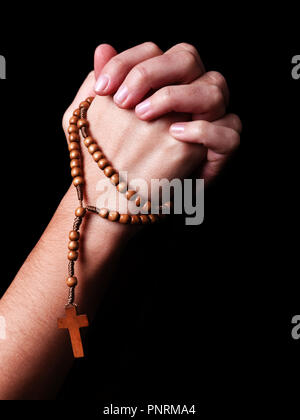 Femme priant mains tenant un chapelet de perles d'une croix ou Crucifix sur fond noir. Femme avec la foi religieuse chrétienne catholique. Profil ou tr Banque D'Images