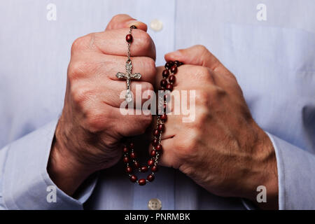 Priant mains tenant un chapelet de perles avec Jésus Christ dans la croix ou Crucifix sur fond noir. Homme mature avec Christian religieuse catholique Banque D'Images