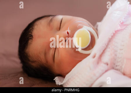 Close up portrait of a cute deux semaines Naissance bebe Fille portant des vêtements en tricot rose tendre, dormir paisiblement avec une tétine, sucette ou factice aka Banque D'Images