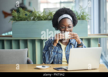 Femme africaine à blogger, la saisie d'un nouveau poste à l'heure du déjeuner dans un café. Banque D'Images