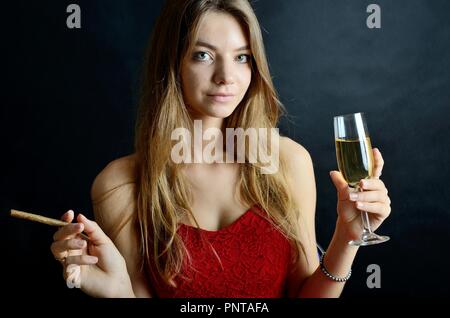 Jeune femme assise avec un cigarillo et verre de vin blanc dans sa main. Femme en robe de soirée rouge. Banque D'Images