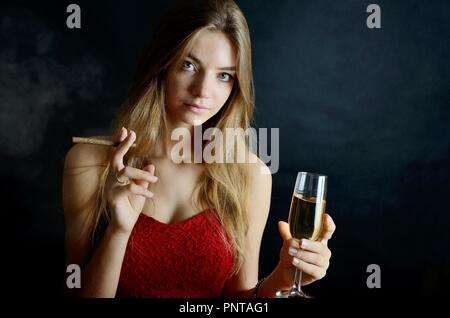 Jeune femme assise avec un cigarillo et verre de vin blanc dans sa main. Femme en robe de soirée rouge. Banque D'Images