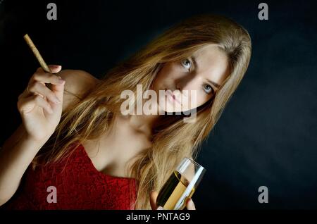 Jeune femme assise avec un cigarillo et verre de vin blanc dans sa main. Femme en robe de soirée rouge. Banque D'Images