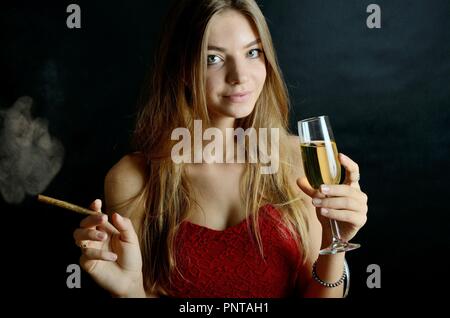 Jeune femme assise avec un cigarillo et verre de vin blanc dans sa main. Femme en robe de soirée rouge. Banque D'Images