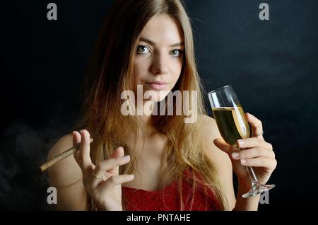 Jeune femme assise avec un cigarillo et verre de vin blanc dans sa main. Femme en robe de soirée rouge. Banque D'Images