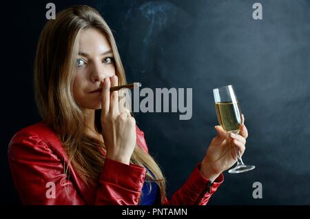 Jeune femme assise avec un cigarillo et verre de vin blanc dans sa main. Woman in red jacket. Banque D'Images