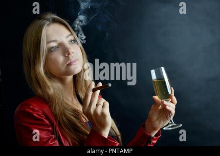 Jeune femme assise avec un cigarillo et verre de vin blanc dans sa main. Woman in red jacket. Banque D'Images