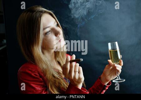 Jeune femme assise avec un cigarillo et verre de vin blanc dans sa main. Woman in red jacket. Banque D'Images