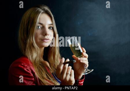 Jeune femme assise avec un cigarillo et verre de vin blanc dans sa main. Woman in red jacket. Banque D'Images