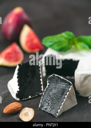 Camembert noir inhabituel avec moisissure blanche.cuisine moderne très tendance, de repas, de l'alimentation.Vue rapprochée du slice noir bio camembert, basilic vert frais, figues, noix sur fond noir.Copy space.Vertical Banque D'Images