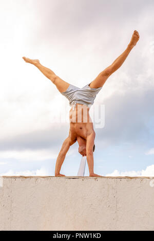 L'homme se tient sur ses mains contre un beau ciel bleu Banque D'Images
