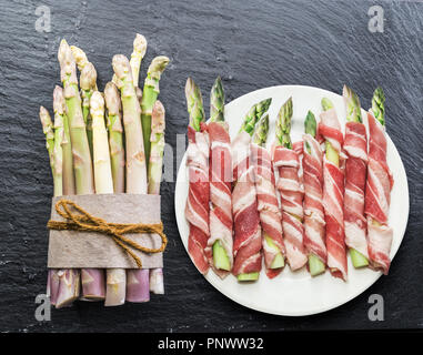 Les pousses d'asperges vertes jambon enveloppé dans l'arrière-plan sur le graphite. Vue d'en haut. Banque D'Images