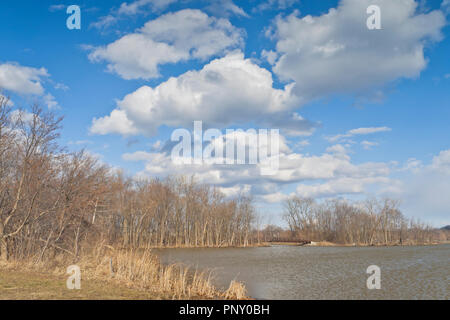 Puffy nuages blancs se détachent sur un ciel bleu au-dessus d'un pont au-dessus d'une partie de Creve Coeur Lake sur un soir venteux au début du printemps. Banque D'Images