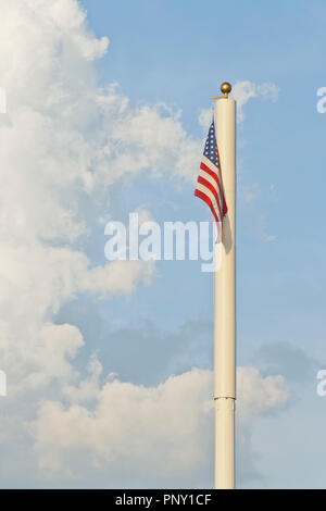 Un drapeau américain est suspendu au sommet d'un poteau avec un immense nuage Cumulus déchiquetés, et ciel bleu en arrière-plan. Banque D'Images