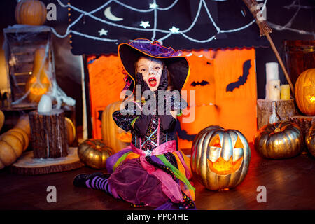 Happy Halloween. Un peu de belle fille dans un costume de sorcière célèbre à la maison dans un intérieur avec des citrouilles et carton magic house sur l'arrière-plan Banque D'Images