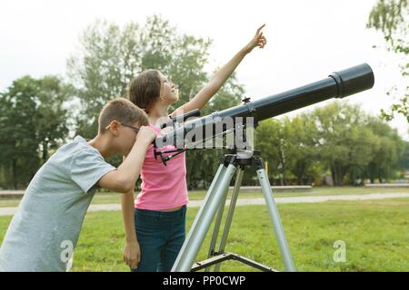 Adolescents Enfants avec Hubble regardez le ciel dans la nature. Banque D'Images