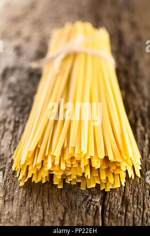 Long ruban plat brut appelé pâtes Fettuccini ficelés sur bois rustique (très faible profondeur de champ, se concentrer sur l'avant de la pasta brins) Banque D'Images