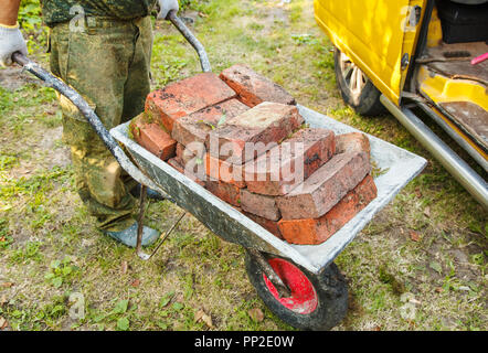 Travailleur est le transport d'une brique dans une brouette outdoor le jour d'été Banque D'Images