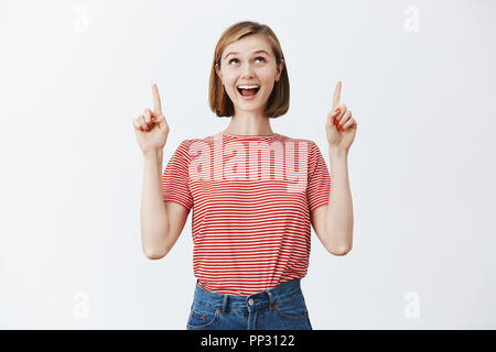 Bientôt je vais être dans l'avion en route vers la mer. Portrait de charmant excité et heureux mignon femelle blonde avec coupe courte en t-shirt à rayures, à la joie et pointant vers le haut avec expression rêveuse Banque D'Images