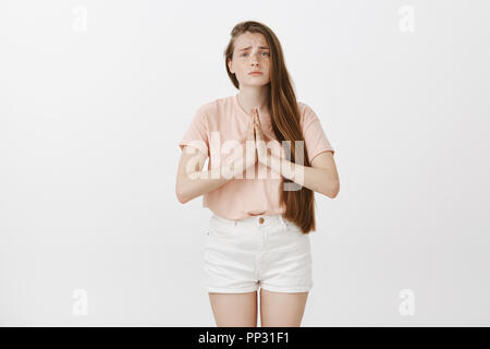 Merci de m'aider un ami. Silly contrarié caucasian woman with freckles dans vêtement élégant, tenant les mains en prière et de froncer tout en posant pour la faveur et la mendicité pour obtenir des conseils, de l'article sur fond gris Banque D'Images