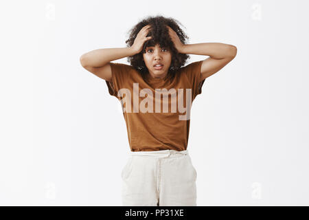 Studio shot of silly et timide bon-à la femme à la peau sombre élève être bouleversés et troublés d'avoir aucune idée de comment résoudre des problèmes à la main de panique sur la tête et les sourcils mécontent Banque D'Images