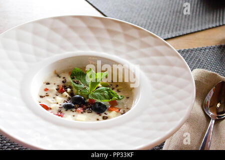 Bon matin, le petit-déjeuner et des aliments sains - concept d'avoine porridge savoureux avec des fraises, les feuilles de menthe, de bleuets et de chocolat en blanc bol plat Banque D'Images
