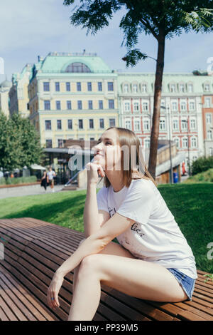 Portrait d'une jeune femme en chemise blanche, assise sur un banc de bois dans un parc au centre de Moscou, en Russie, par une chaude journée ensoleillée Banque D'Images