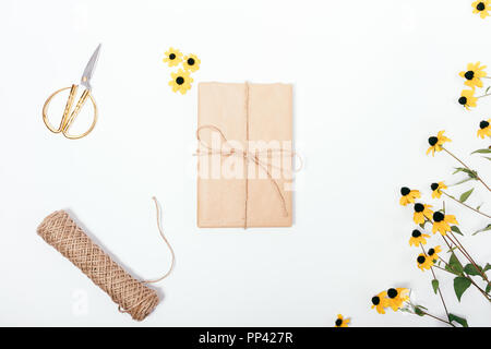 Tout cadeau enveloppé dans du papier craft marron près de fleurs jaunes, de la ficelle et des ciseaux, vue d'en haut. Télévision Floral composition de laïcs présents sur emballés à la main Banque D'Images