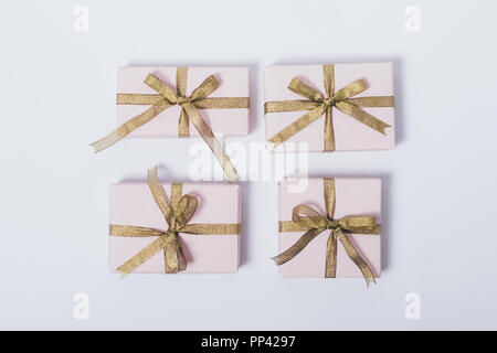 Un minimum de mise à plat composition de paniers et préparé des cadeaux pour les vacances. Close-up quatre boîtes cadeau rose avec des rubans d'or et d'arcs sur blanc retour Banque D'Images