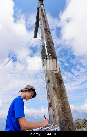 Randonneur Venet : Jeune homme garçon écrit dans sommet livre à mountain sommet Venet, Glanderspitze sommet cross, région TirolWest, Tirol, Tyrol, Autriche Banque D'Images