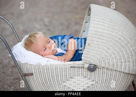 Peu de nouveau-né garçon, dormir dans ancienne rétro poussette en forêt, le temps d'automne. Posés bébé dans la PRAM, rétro, vintage baby stroller Banque D'Images