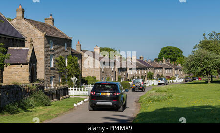 Ligne de cottages traditionnels en pierre en face du village pittoresque en communauté rurale, 4 Land Rover passant - East Witton, North Yorkshire, Angleterre, Royaume-Uni. Banque D'Images