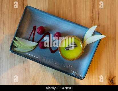 Une Tarte Key Lime avec quelques framboises et les tranches de pommes sur un plat rectangulaire bleue Banque D'Images